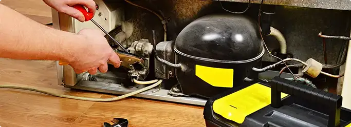 Refrigerator repair technician fixing the compressor and wiring in Roy, UT