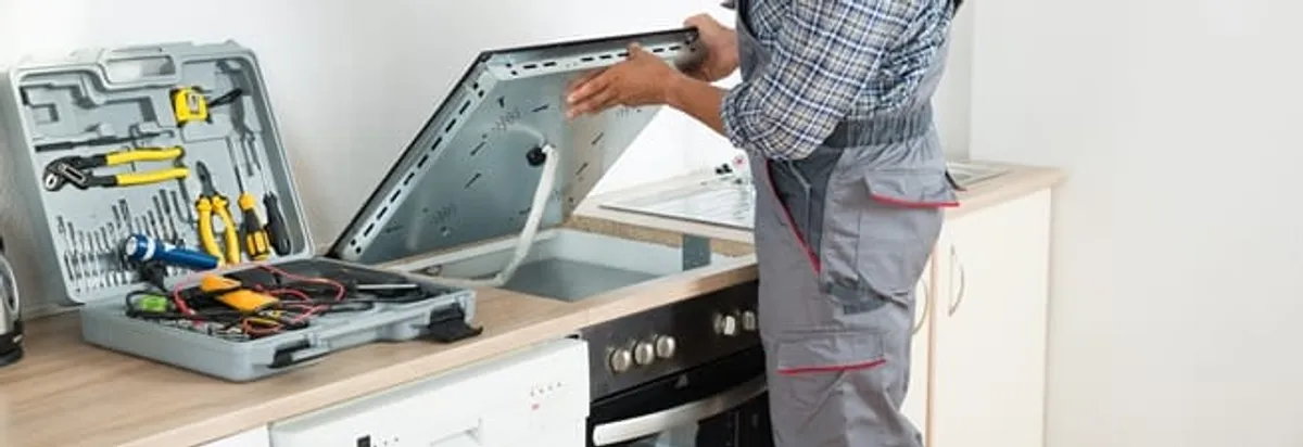 Cooktop repair technician lifting a built-in stovetop for service in Ogden, UT