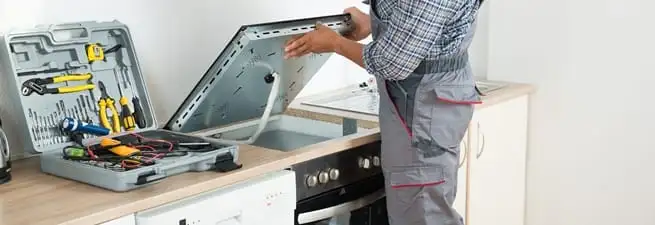 Cooktop repair technician lifting a built-in stovetop for service in Ogden, UT