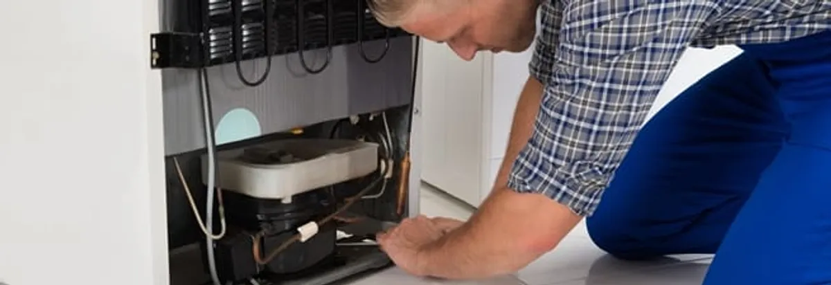 Refrigerator repair technician servicing the compressor and condenser area in Ogden, UT