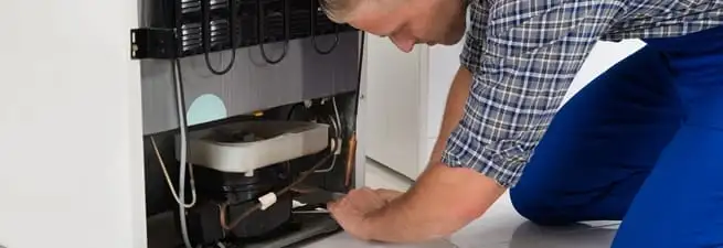 Refrigerator repair technician servicing the compressor and condenser area in Ogden, UT
