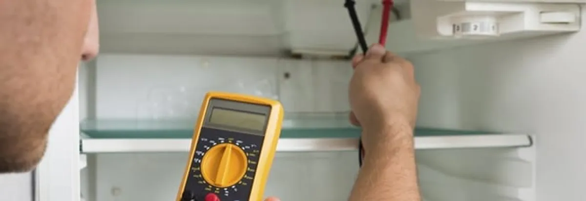 Refrigerator repair technician testing electrical components with a multimeter in Ogden, UT