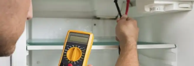 Refrigerator repair technician testing electrical components with a multimeter in Ogden, UT