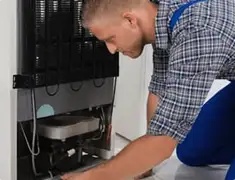 Refrigerator repair technician servicing the compressor and condenser area in Ogden, UT